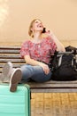 Female traveler with luggage sitting on bench and talking on cellphone Royalty Free Stock Photo