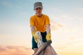 Portrait of female volunteer in rubber gloves puts a dirty plastic bottle in bag with garbage. Sunset sky on the