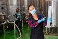 Woman vintner in mask checking wine process