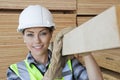 Portrait of female worker carrying wooden plank on shoulder