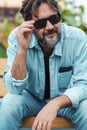 Portrait of fifty years old mature young man sitting and resting touching sunglasses and smiling. Bearded caucasian male in