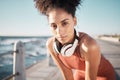 Portrait, fitness and black woman tired, ocean and runner with headphones, focus and determined for goal. African