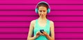 Portrait of fitness smiling young woman in headphones listening to music with smartphone on pink background Royalty Free Stock Photo