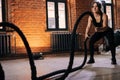 Portrait of fitness young athletic woman with strong beautiful body in black activewear exercising with battle ropes Royalty Free Stock Photo