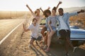 Portrait Of Five Friends Standing By Convertible Classic Car On Road Trip