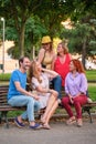 Five mature adults talking and laughing sitting on a bench in a park.