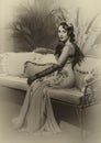 Portrait flapper woman in twenties old style sitting on sofa couch. Long evening retro dress ostrich feather boa cold Royalty Free Stock Photo