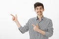 Portrait of flirty funny european male model with moustache and beard in striped shirt, pointing left with finger gun Royalty Free Stock Photo