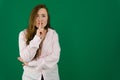 Portrait of flirty young woman making silence gesture over green background. Caucasian lady wearing shirt posing with Royalty Free Stock Photo