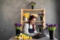 Portrait florist in a blue work apron working in her own flower shop, using a laptop, organizing logistics and