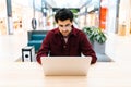 Portrait of focused bearded businessman in glasses sitting on sofa in shopping mall typing working on laptop. Royalty Free Stock Photo