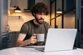 Portrait of focused bearded young business man holding in hand cup with morning coffee sitting at table with laptop Royalty Free Stock Photo