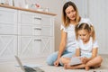 Portrait of focused little primary school girl writing in copybook sitting on floor with loving young mother. Royalty Free Stock Photo