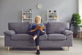 Portrait of a focused senior woman sitting on a sofa and reading an interesting book.