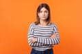 Portrait of focused serious young woman with brown hair in long sleeve striped shirt. isolated on orange background