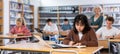 Portrait of focused teenage female pupil sitting at desk studying in library with classmates Royalty Free Stock Photo