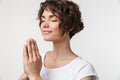 Portrait of focused woman with short brown hair in basic t-shirt keeping palms together and praying