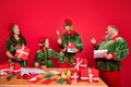 Portrait of four trendy cheerful elfs preparing gift list order dream delivery isolated over bright red color background