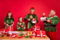 Portrait of four trendy cheerful elfs santa helper preparing gift list order isolated over bright red color background