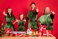 Portrait of four trendy friends friendship elfs santa helper showing thumbup isolated over bright red color background