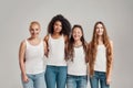 Portrait of four young diverse women wearing white shirts and denim jeans smiling at camera while posing together