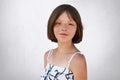 Portrait of freckled little girl with dark short hair, hazel eyes and thin lips wearing black and white dress, posing at camera ag Royalty Free Stock Photo