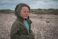 Portrait of freckles handsome blond boy on beach on windy day. Alone child with hood walking on sandy beach. Autumn.