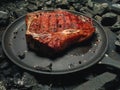 Portrait of fried steak in a frying pan among pieces of coal.