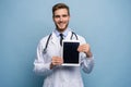 Portrait of friendly doctor presenting empty digital tablet screen. Isolated on light blue. Royalty Free Stock Photo