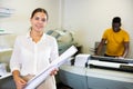 Portrait of friendly female employee of printing house with stack of notebooks in her hands