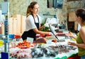 Portrait of friendly female fishmonger showing raw European bass to woman behind counter of seafood store Royalty Free Stock Photo