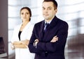 Portrait of a friendly middle aged businessman in a dark blue suit, standing with crossed arms together with a colleague Royalty Free Stock Photo