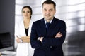 Portrait of a friendly middle aged businessman in a dark blue suit, standing with crossed arms together with a colleague Royalty Free Stock Photo