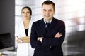 Portrait of a friendly middle aged businessman in a dark blue suit, standing with crossed arms together with a colleague Royalty Free Stock Photo