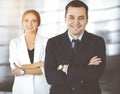 Portrait of a friendly middle aged businessman in a dark blue suit, standing with crossed arms together with a colleague Royalty Free Stock Photo