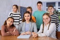 Portrait of positive group of pupils with female teacher sitting in schoolroom