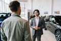 Portrait of friendly professional car dealer selling new automobile to unrecognizable male client explaining Royalty Free Stock Photo