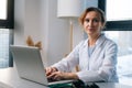 Portrait of attractive female doctor wearing white coat sitting at table with laptop computer and looking camera. Royalty Free Stock Photo