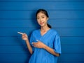 Portrait of friendly, smiling confident Asian woman doctor or nurse in blue scrubs suit pointing fingers. Royalty Free Stock Photo