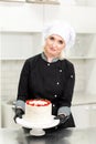 Portrait of friendly smiling female professional confectioner topping a cupcake with cream using a pastry bag Royalty Free Stock Photo