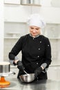 Portrait of friendly smiling female professional confectioner topping a cupcake with cream using a pastry bag Royalty Free Stock Photo