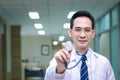 Portrait of friendly smiling senior Asian male doctor in white workwear showing stethoscope to camera, standing in corridor of Royalty Free Stock Photo