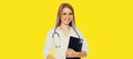 Portrait of friendly smiling young woman doctor with stethoscope and folder of documents on yellow background Royalty Free Stock Photo