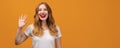 Portrait of friendly woman with wavy redhead, standing waving hand, looking at camera with engaging toothy smile Royalty Free Stock Photo