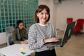 Portrait of friendly young businesswoman in casual clothes holding laptop in hand standing in office smiling looking at Royalty Free Stock Photo