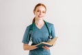 Portrait of friendly young woman doctor in green uniform with stethoscope holding medical book standing and looking at Royalty Free Stock Photo