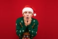 Portrait of a frightened young man in Christmas clothes, wearing a santa hat and a warm winter sweater, with shocked face looking Royalty Free Stock Photo
