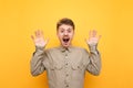 Portrait of frightened young man in glasses and shirt on yellow background, raised his hands in fear and looks into camera with Royalty Free Stock Photo