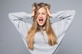 Portrait of a frustrated angry woman screaming out loud and pulling her hair out isolated on the gray background Royalty Free Stock Photo