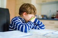 Portrait of frustrated crying sad school kid boy at home making homework. Little child writing with colorful pencils